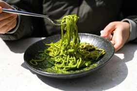 A person twirling forkful of spaghetti coated in pesto sauce on a plate