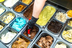 A hand scooping ice cream from a container in a display of various ice cream flavors