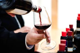 Wine being poured into a glass bottles of wine lined up in the background