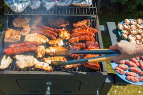 A person grilling various pieces of meat and sausages on an outdoor barbecue