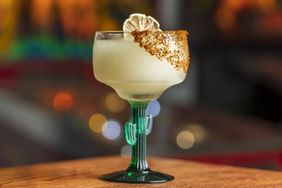 A margarita in a cactusshaped glass with a salted rim and lime garnish
