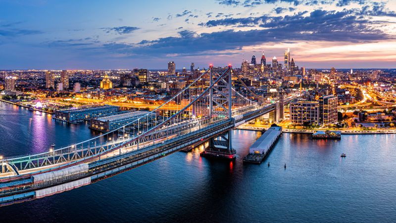 Aerial panorama with Ben Franklin Bridge and Philadelphia skyline in transition from sunset to dusk. Ben Franklin Bridge is a suspension bridge connecting Philadelphia and Camden, NJ.