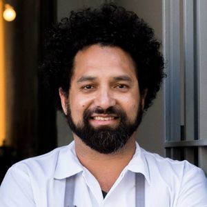 A man with a beard and curly hair wearing a collared shirt smiling at the camera