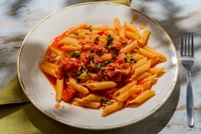 Plate of penne pasta with tomatobased sauce and herbs placed on a green cloth with a fork nearby