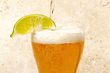 An NA beer brewed by Curious Elixirs being poured into a glass with a lime wedge.