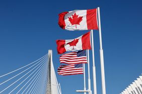 Canadian and American flags on tall poles bridge cables and blue sky in the background