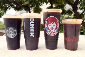 Four branded cold brew coffee cups from chains Starbucks Dunkin Wendys and Chickfila on a table outdoors