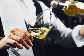 A closeup of a person pouring white wine into a glass