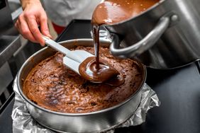 Pouring melted chocolate into a cake batter in a round baking pan