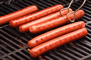 Hot dogs being grilled on a barbecue with tongs