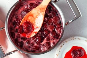 Cooking strawberry jam in a saucepan with a wooden spoon plated jam nearby