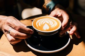 Hands holding a cup of coffee with latte art on the surface placed on a wooden table