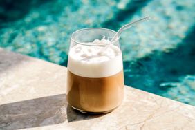 A glass of coffee with cold foam and a straw placed by a poolside