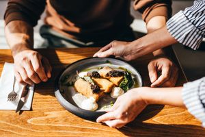 A plate of food with plated items being served or adjusted on a wooden table by someones hands