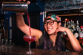 Christine Kim smiling while pouring a drink into a cocktail glass at a bar