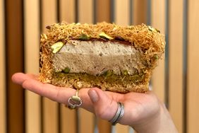 Hand holding a layered dessert topped with nuts and shredded pastry