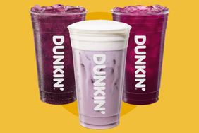 Three Dunkin drinks in clear plastic cups with lids arranged in a group on a yellow background
