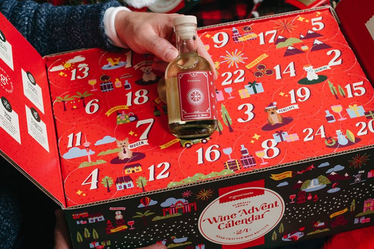 A person holding a small wine bottle in front of a wine advent calendar featuring numbered sections