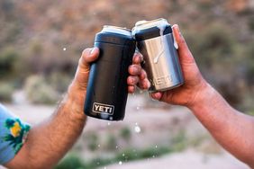 Two hands holding insulated Yeti can holders toasting with drinks outdoors
