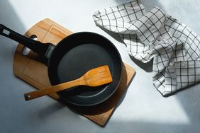 Cast iron skillet on a wooden cutting board with a wooden spatula and a checkered kitchen towel nearby