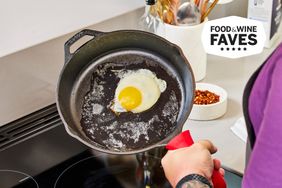 A person holding a skillet with a fried egg inside on a stovetop
