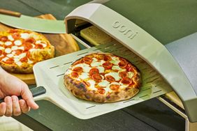 A pizza being removed from an outdoor pizza oven on a pizza peel
