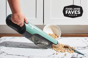 A person vacuums spilled cereal from a floor with a handheld vacuum.