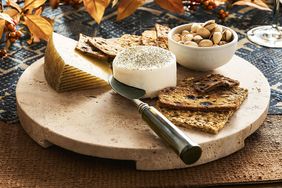 A cheese board presentation with a selection of cheeses crackers and nuts alongside a serving knife placed on a round marble platter