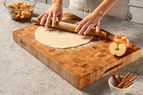 Rolling out dough on a wooden cutting board surrounded by apples and cinnamon sticks