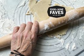 A person flattens a piece of dough on a floured surface with a rolling pin.