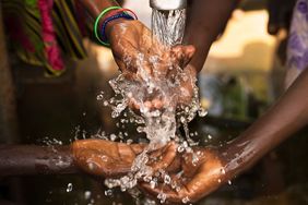 Hands being washed under running water outdoors emphasizing clean water and sanitation