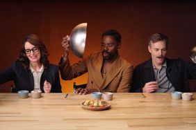 Tina Fey Colman Domingo and Will Forte seated side by side at a table with food dishes interacting during an event