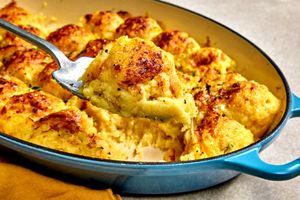 Spoon serving a portion of French onion mashed potatoes from a baking dish with golden topping