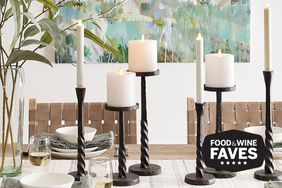 A dining table setup featuring flameless wax pillar candles on twisted metal holders surrounded by tableware and decorative plants