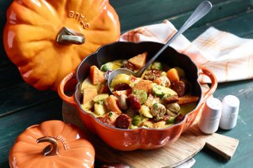 A pumpkinshaped dish containing a prepared meal with a ladle on a wooden table