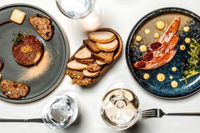 Plated gourmet dishes on a table with bread fish steak and sauces displayed decoratively