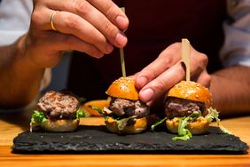Mini sliders being garnished on a slate serving plate