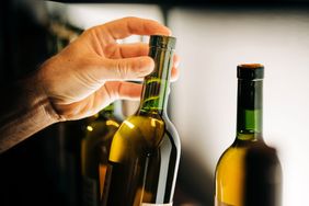 A hand selecting a wine bottle from a shelf with other bottles