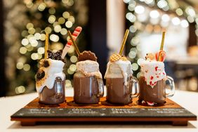 Four mugs of hot chocolate each with unique toppings displayed on a tray