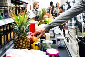 Groceries on a checkout conveyor belt in a supermarket with people in the background shopping