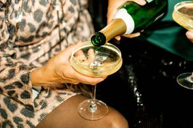 Champagne being poured into a coupe glass held by a person in formal attire