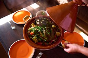 A tagine dish being served at a table set with plates and utensils