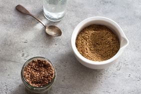 Flax seeds in a glass jar, ceramic a bowl of ground flax and water for soaking the flax and making healthy meals on a gray textured background.