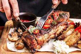 Grilled ribs being sliced paired with side dishes