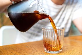 Pouring coffee from a carafe into a glass on a wooden table