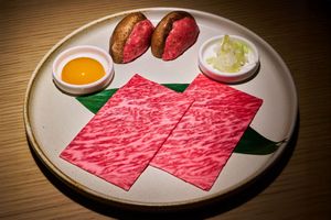 A plate with slices of Wagyu beef a raw egg yolk and garnishes presented on a decorative leaf