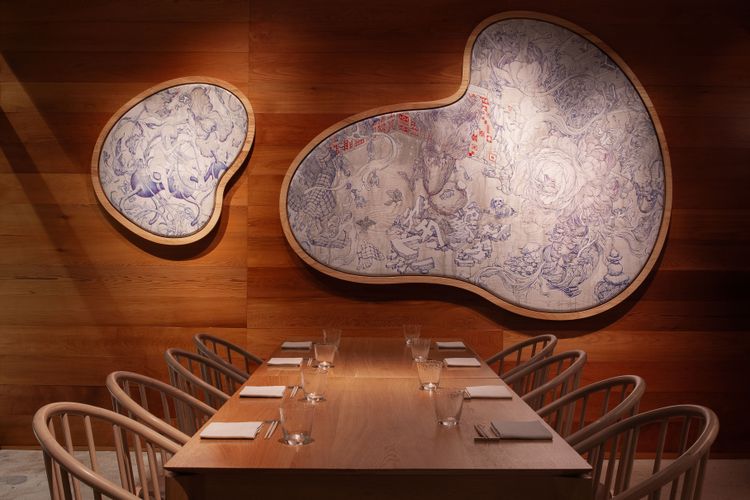A wooden dining table with chairs two beanshaped artworks on a wooden wall