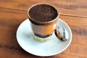 A glass of kopi tubruk on a saucer with a spoon beside it a traditional Indonesian coffee
