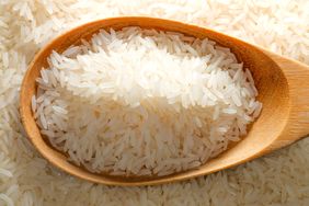 A scoop of rice in a wooden spoon on a pile of rice