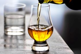 A glass being filled with whiskey on a table with a water glass in the background